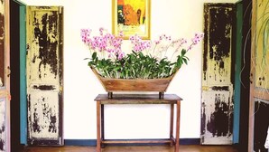 A room with a wooden table holding a flower arrangement, two doors with peeling paint, and a framed artwork on the wall.