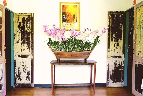 Une pièce avec une table en bois sur laquelle est disposé un arrangement floral, deux portes dont la peinture s’écaille et une œuvre d’art encadrée accrochée au mur.