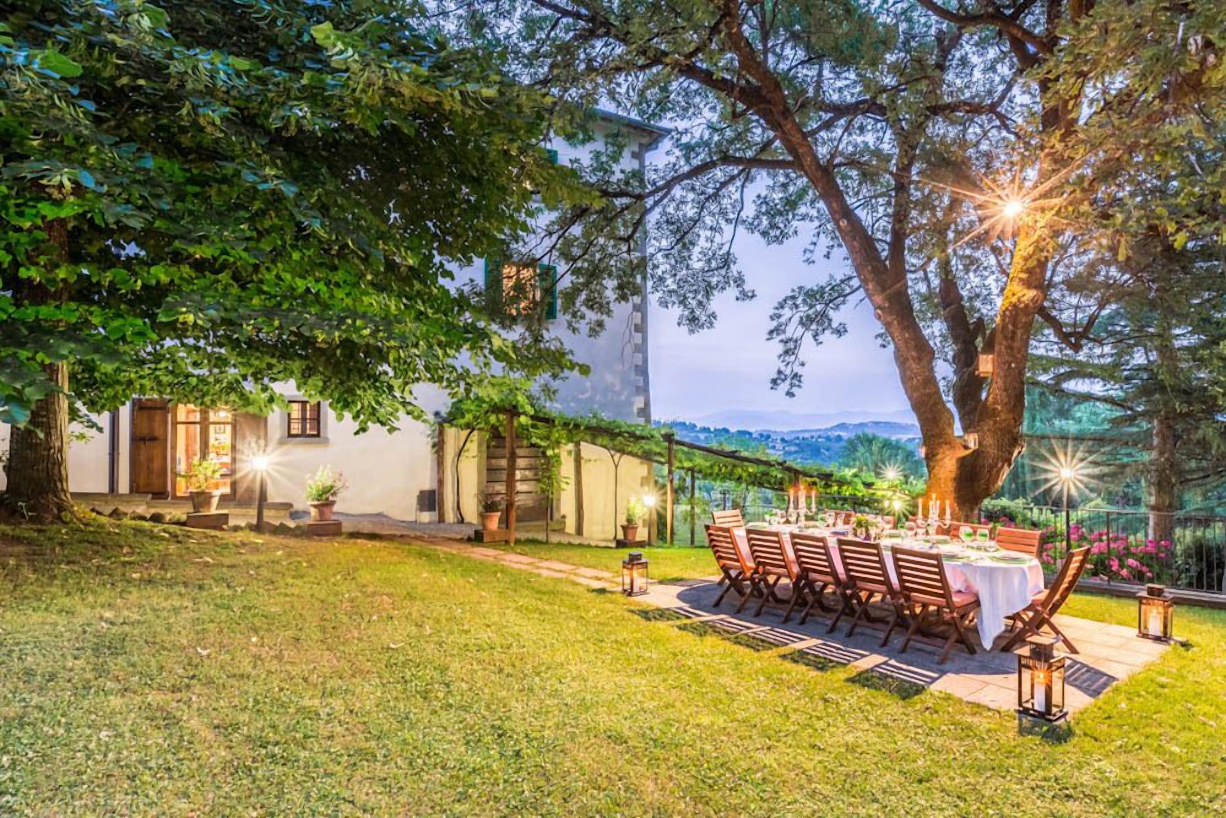An outdoor dining area with a table set for four, surrounded by chairs, under a large tree.