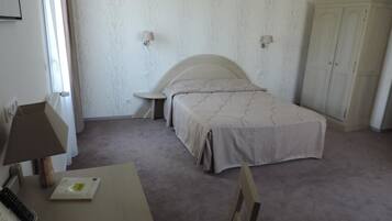 A bedroom with a bed, a desk, a chair, a wardrobe, and two wall-mounted lamps.
