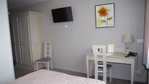 Una habitación de hotel con una cama, un escritorio con una silla, un televisor y un cuadro en la pared.