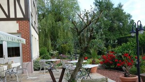 Un patio al aire libre con suelo de piedra, sillas de metal, una mesa y plantas en macetas.
