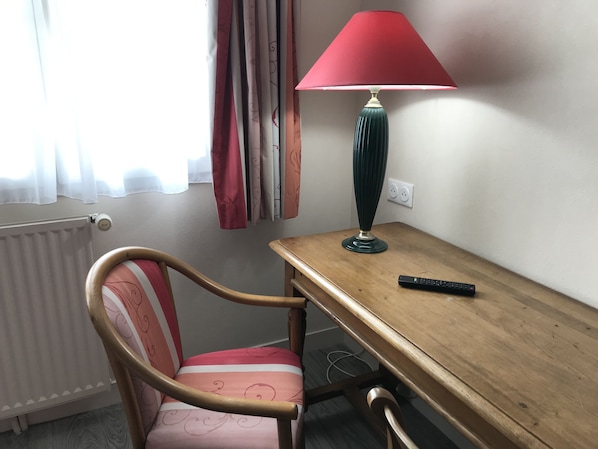 A small room with a wooden desk, a chair, a red lamp, and a remote control.