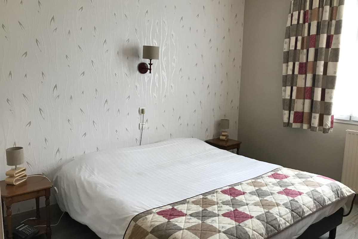 A neatly made bed with a quilt, a bedside table with a lamp, and a wall-mounted light fixture.