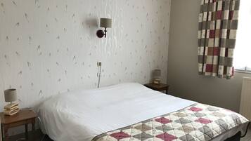 Un lit bien fait, avec une couverture, une table de chevet avec une lampe et un luminaire fixé au mur.