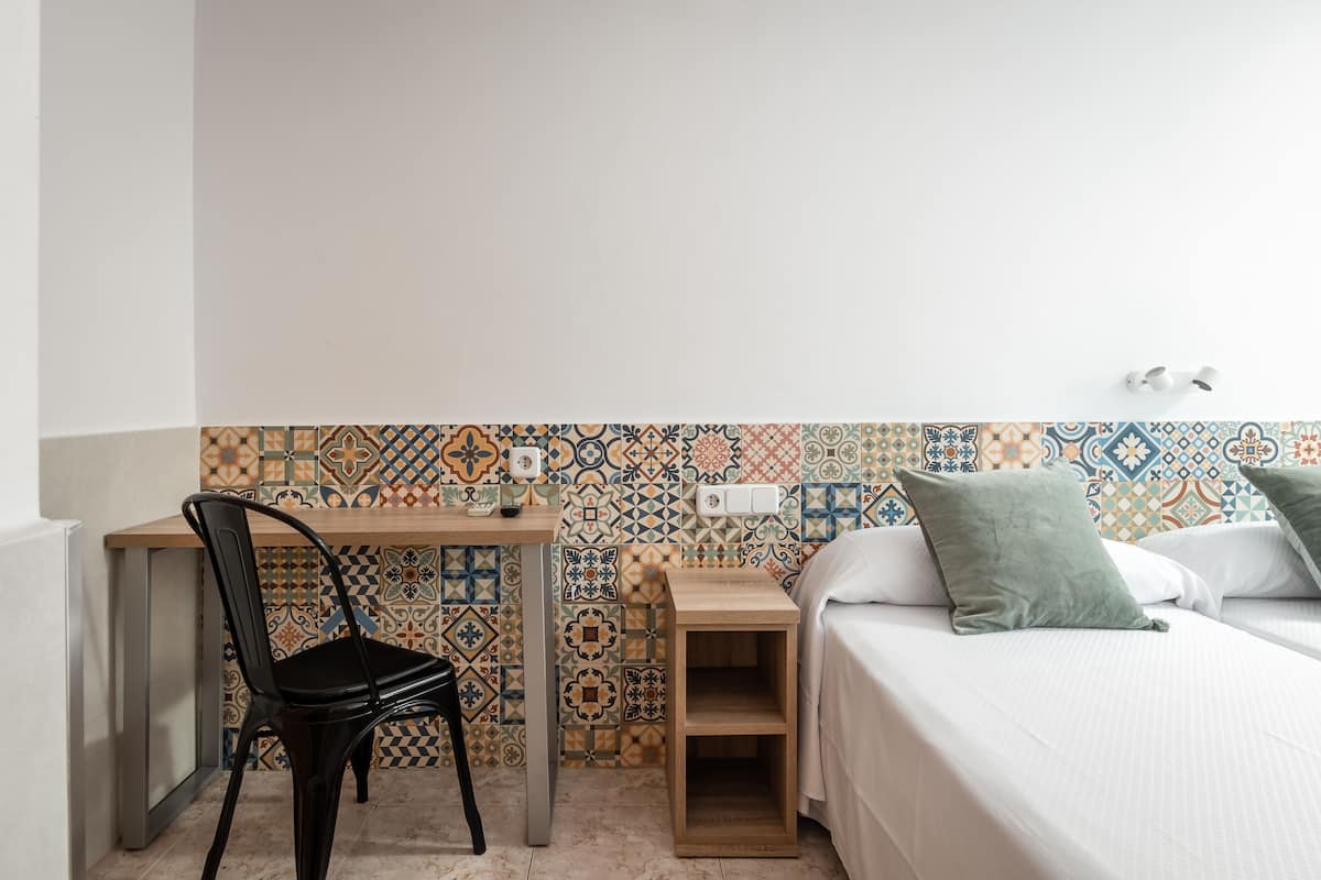 A small, neatly arranged room with a bed, a desk, and a chair.