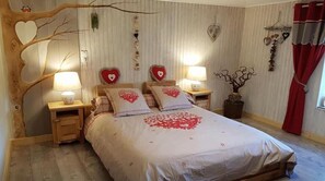 Un dormitorio con una cama grande, dos mesitas de noche, decoraciones con forma de corazón y un diseño de rama de árbol en la pared.
