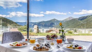 Una mesa lista para el desayuno, con platos de comida, bebidas y vistas a las montañas.