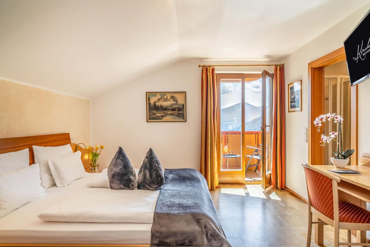 Habitación de hotel con cama, escritorio y vistas a montañas desde la puerta.