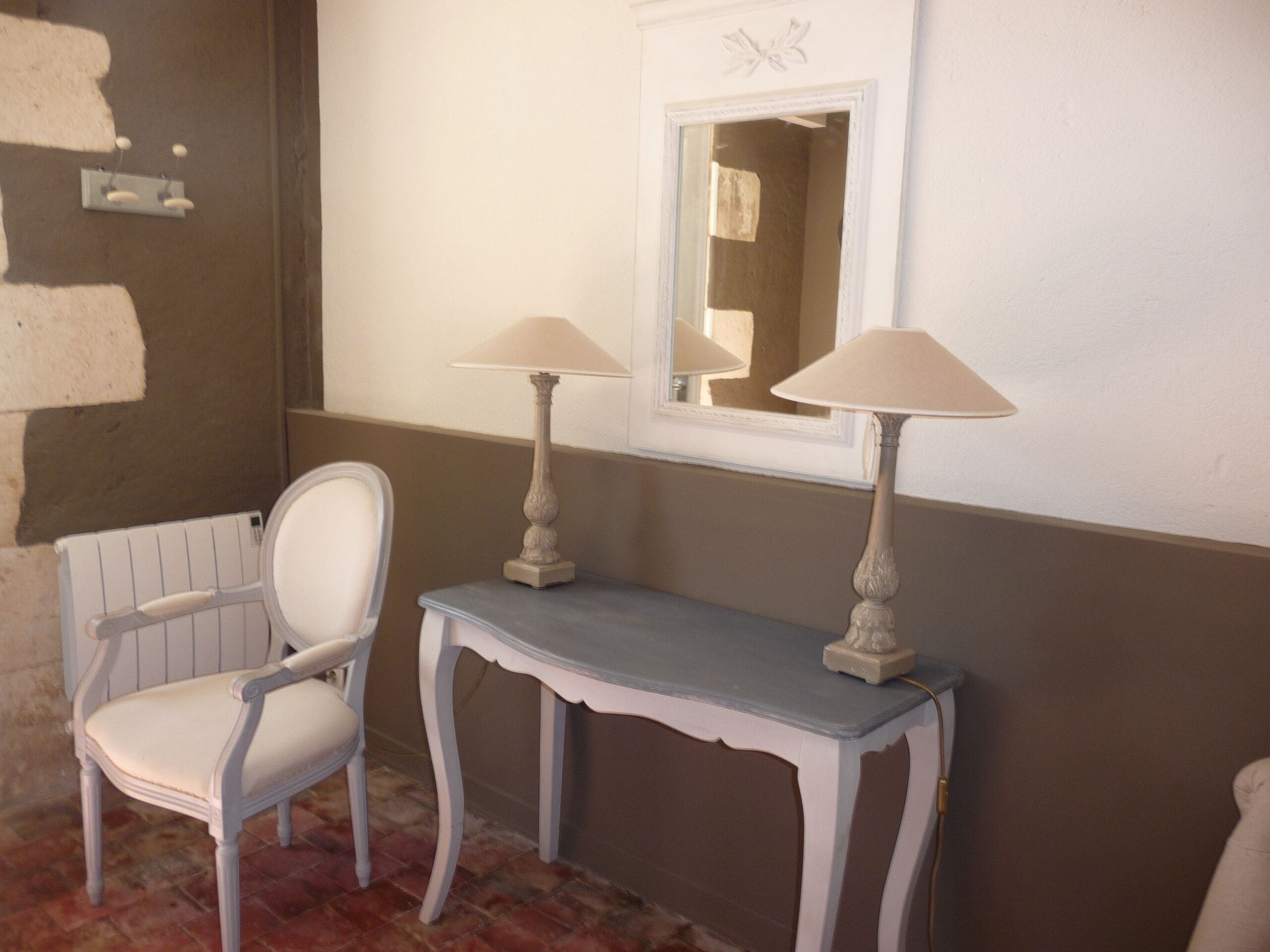 Un baño con una silla blanca, un tocador con espejo y dos lámparas de pared.