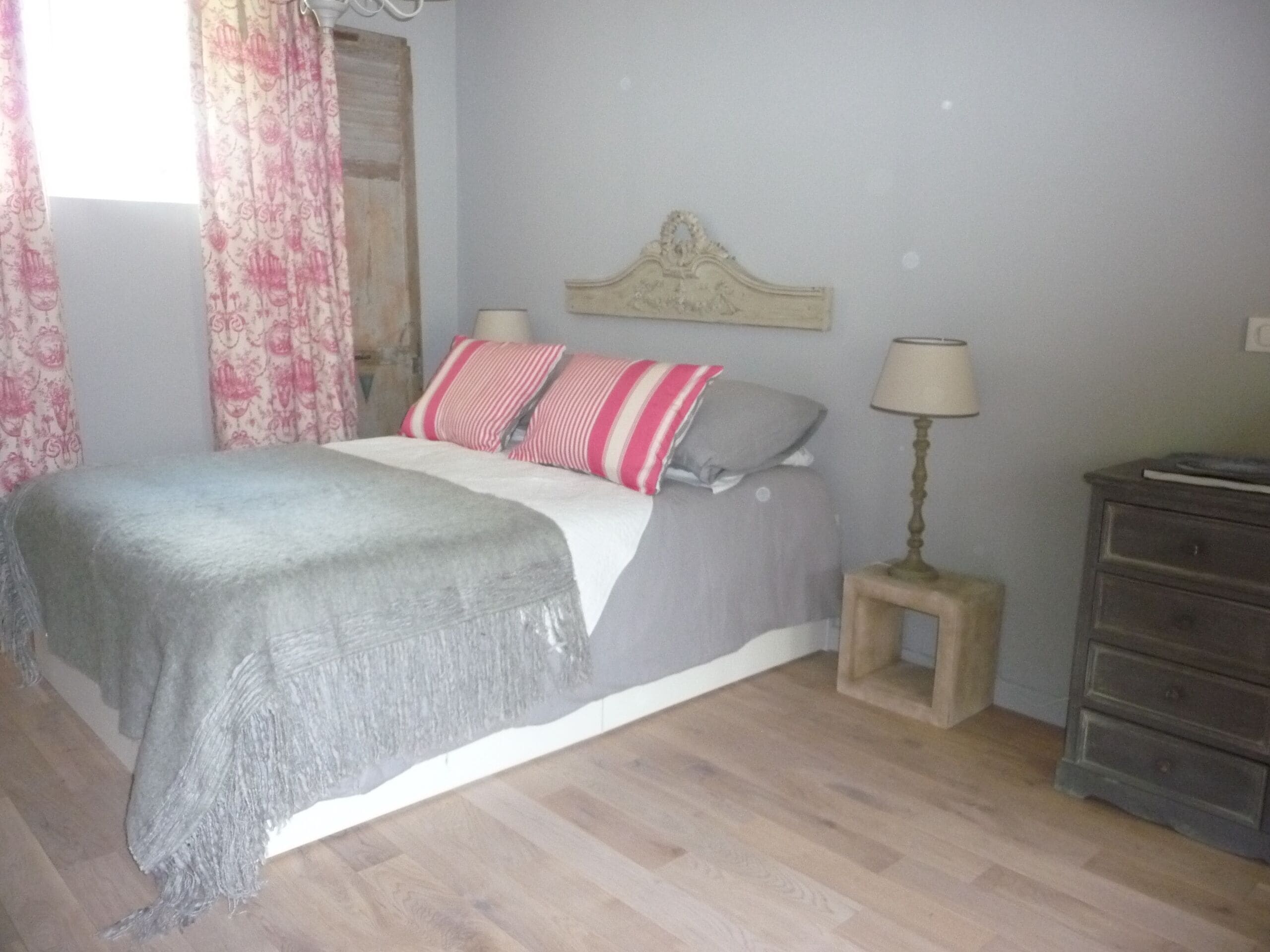 A bedroom with a bed, a dresser, a lamp, and a window with curtains.