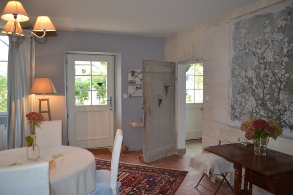Una habitación con una mesa redonda, una silla, una mesita de madera, una puerta y una pared decorada con una pintura floral.