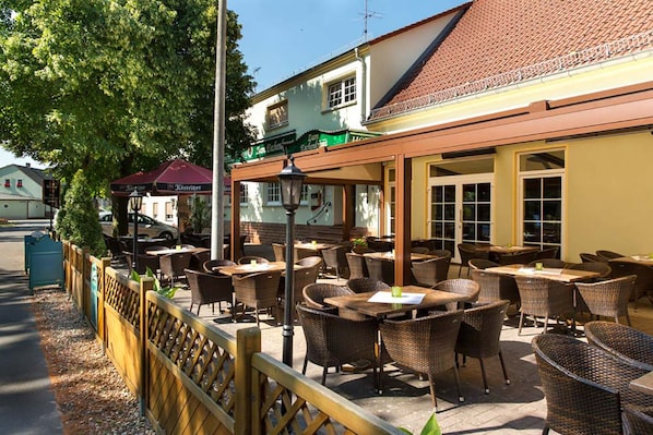 An outdoor cafe with wicker furniture and a wooden fence. - Hotel und Gasthaus zum Eichenkranz (Luckenwalde)