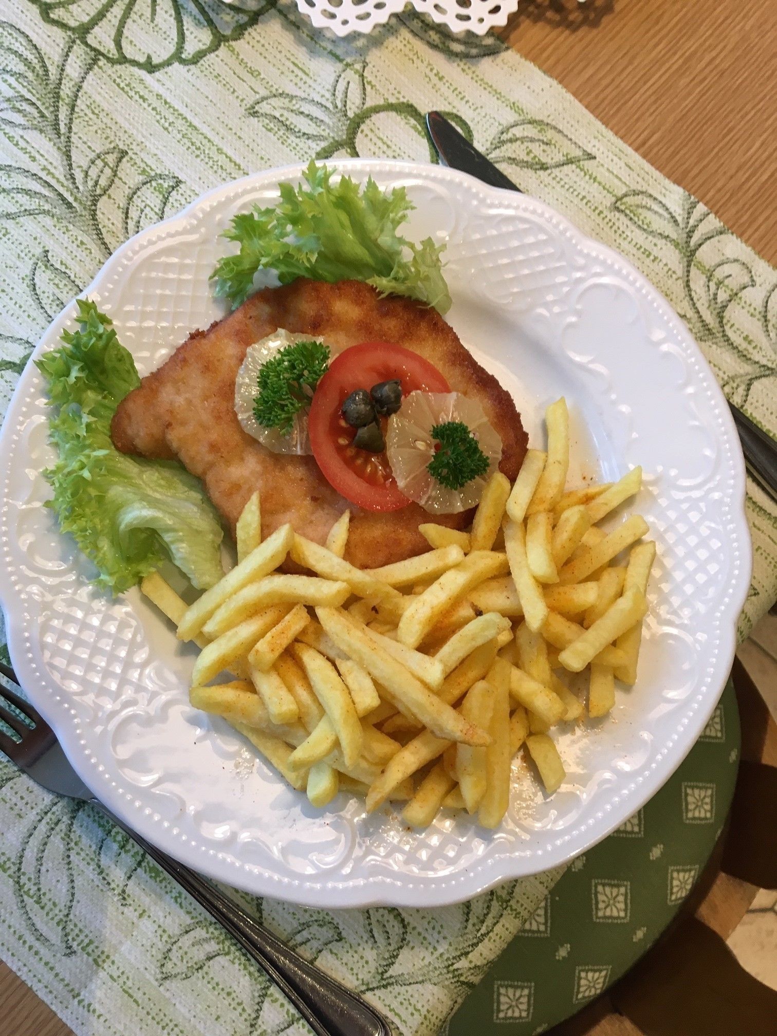 A plate of food with a breaded cutlet, fries, lettuce, and garnishes.