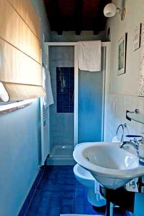 A bathroom with a white sink, a shower, and a window with a towel hanging on the door. - Verdidea - SOTTO COLLE (Montelupo Fiorentino)