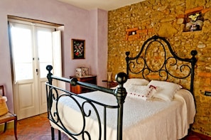 A bedroom with a stone wall, a bed with white linens, a wooden nightstand, and a chair. - Verdidea - SOTTO COLLE (Montelupo Fiorentino)