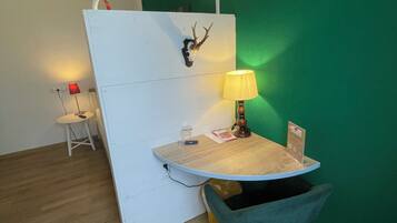 Ein Zimmer mit grüner Wand, einer weißen Trennwand, einem runden Tisch mit Lampe, einem Stuhl und einem kleinen Tisch mit roter Lampe.