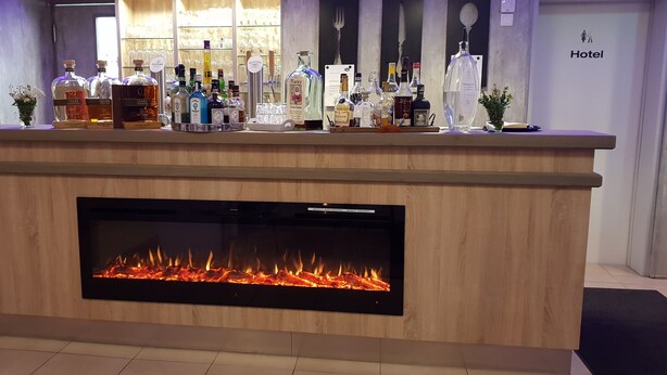Uma área de recepção de hotel com um balcão de madeira, diversos frascos de bebidas alcoólicas e uma lareira.