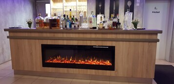 Ein Hotel-Rezeptionsbereich mit Holztresen, verschiedenen Spirituosenflaschen und einem Kamin.