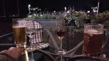 Un tavolo con tre bicchieri di birra e un bicchiere di vino, apparecchiato all'aperto di sera.
