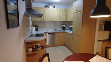 Cocina compacta con armarios de madera, un lavamanos de acero inoxidable, lavavajillas y microondas. Hay un estante pequeño con frascos y un marco de fotos en la pared.