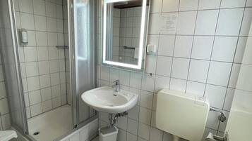 Un baño con ducha, lavamanos, inodoro y espejo.