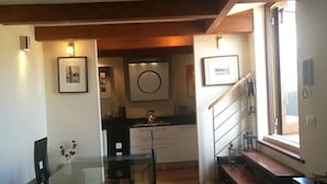 Cozinha moderna com vigas de madeira, área de jantar com mesas de vidro e escada com vista para o exterior.