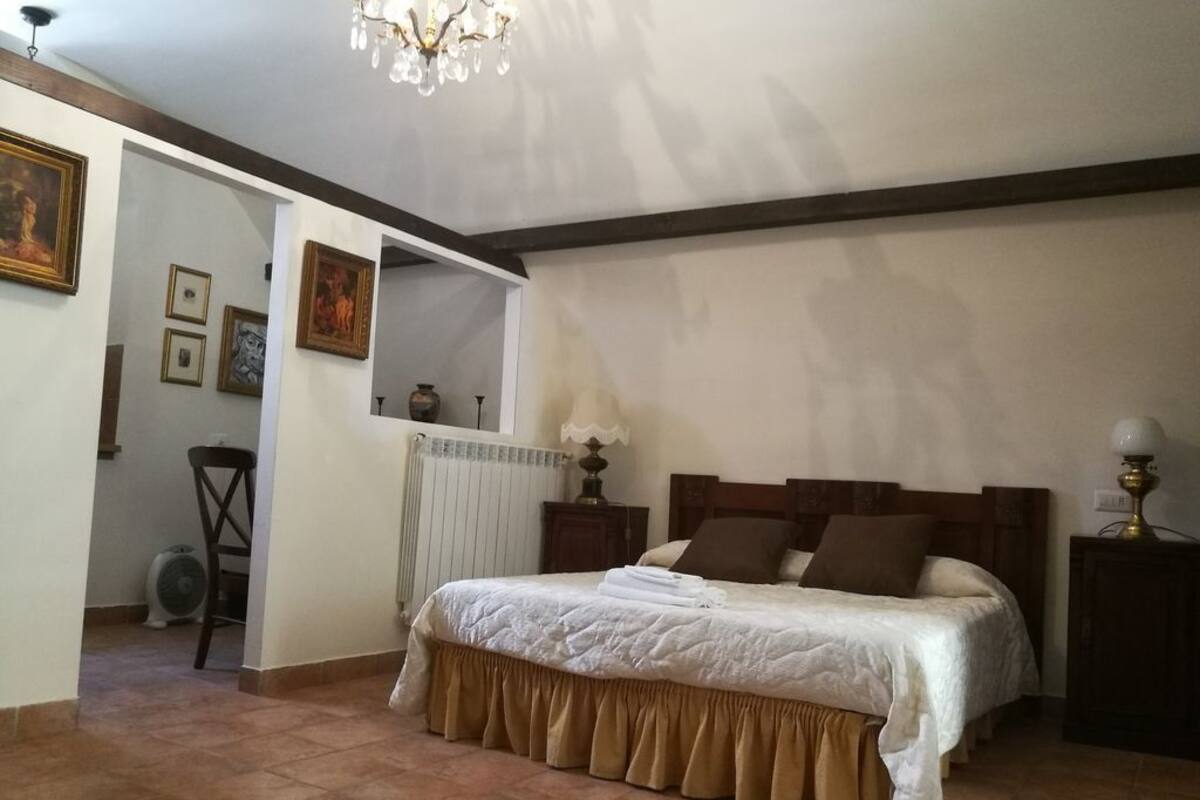 A bedroom with a large bed, a wooden headboard, a chandelier, and a radiator.