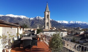A terrace with outdoor furniture, a view of a church with a bell tower, and snow-capped mountains in the background. - Legacy (Sulmona)