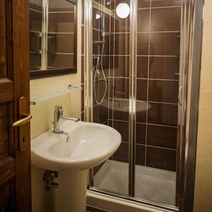 A bathroom with a glass-enclosed shower, a sink, and a mirror. - Legacy (Sulmona)