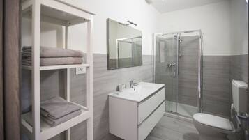 A modern bathroom with a glass shower enclosure, a white sink, and a built-in shelf with folded towels.