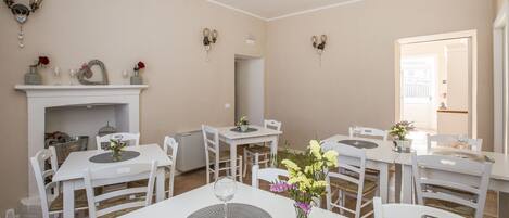 Un comedor con mesas y sillas blancas, una chimenea y apliques de pared.