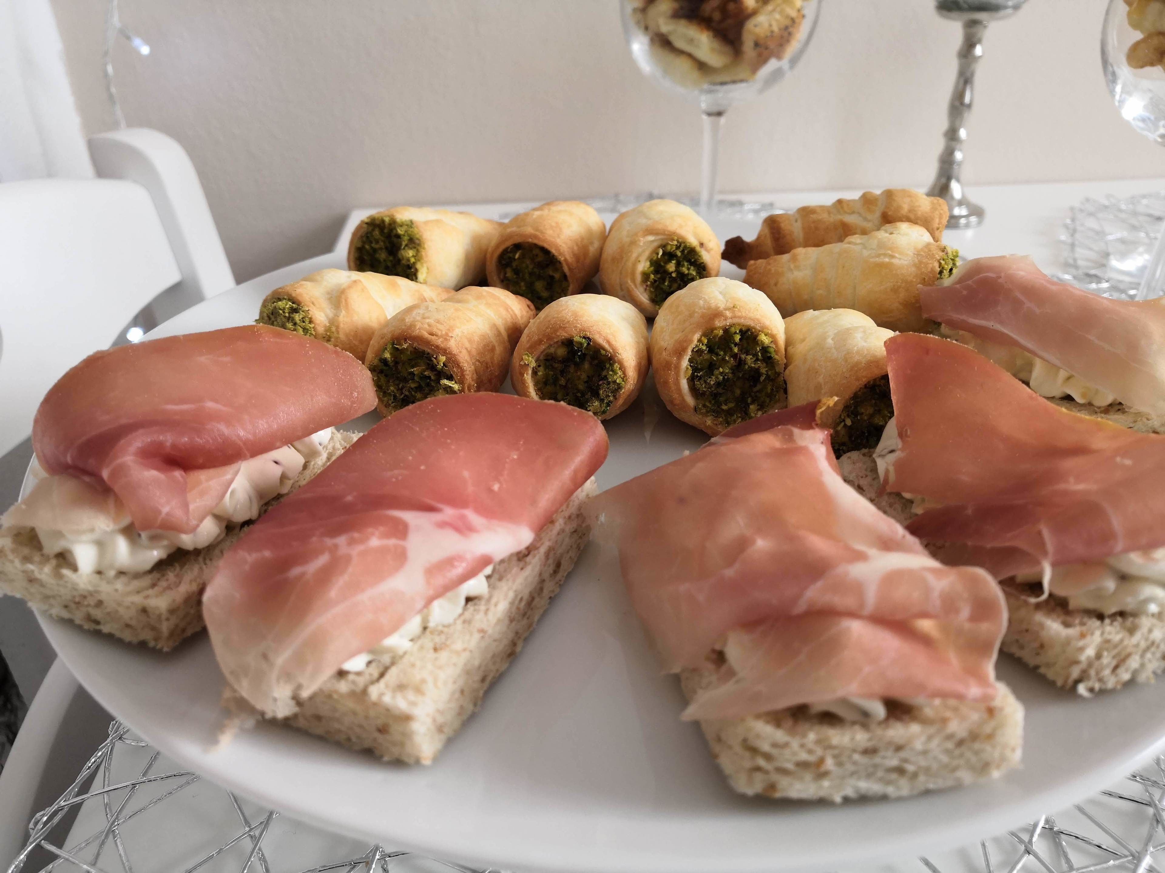 Um prato de sanduíches com presunto e uma variedade de doces.