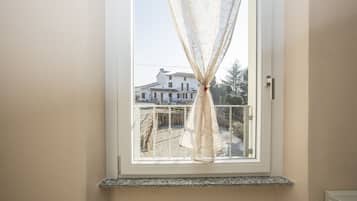A window with a sheer curtain, a white door, and a view of a residential building with a balcony.