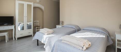 A bedroom with two beds, a desk, a chair, a wardrobe, and a television.