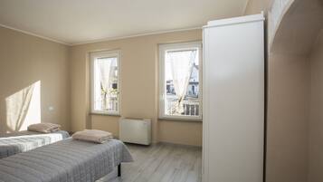 Un dormitorio con dos camas, un radiador y ventanas amplias.