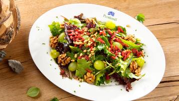 Ensalada de hojas verdes variadas con nueces, uvas y bayas rojas sobre una mesa de madera.