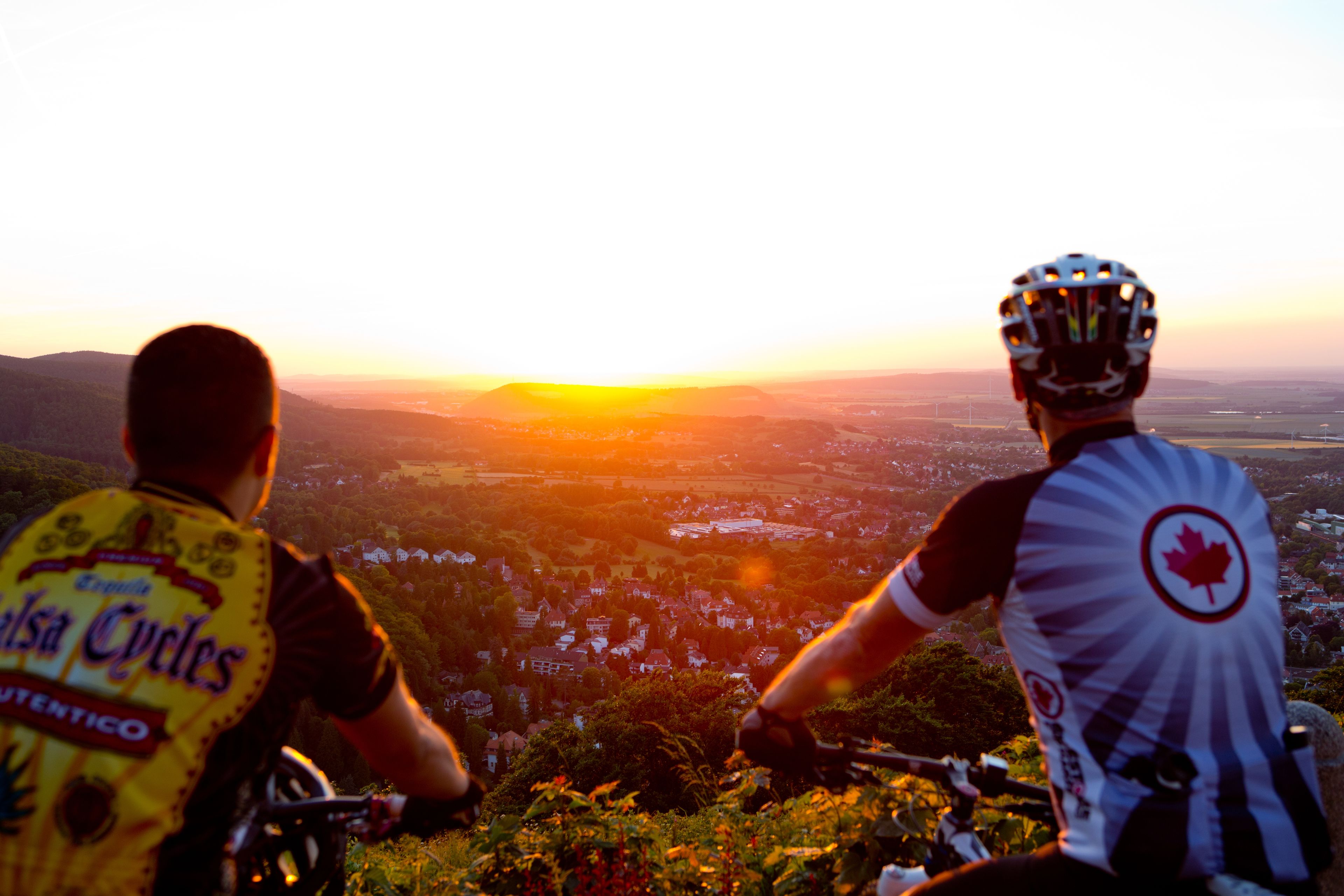 Zwei Radfahrer überblicken ein Tal bei Sonnenuntergang, hoch in den Bergen.