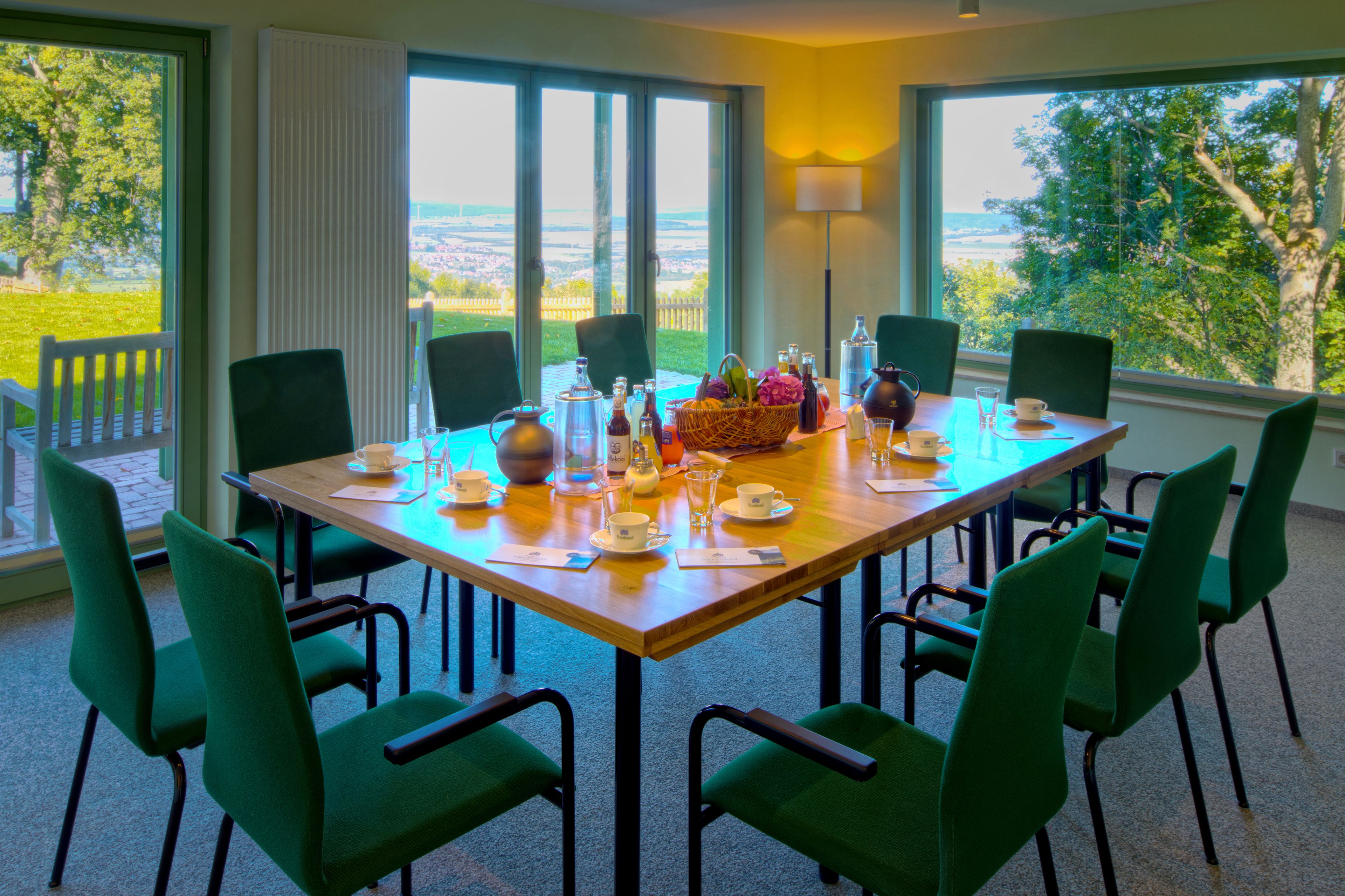 A dining table set for six with chairs, a view of the outdoors, and a lamp on the wall.
