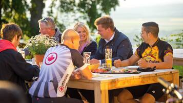 A group of people seated around a wooden table outdoors, engaged in conversation.