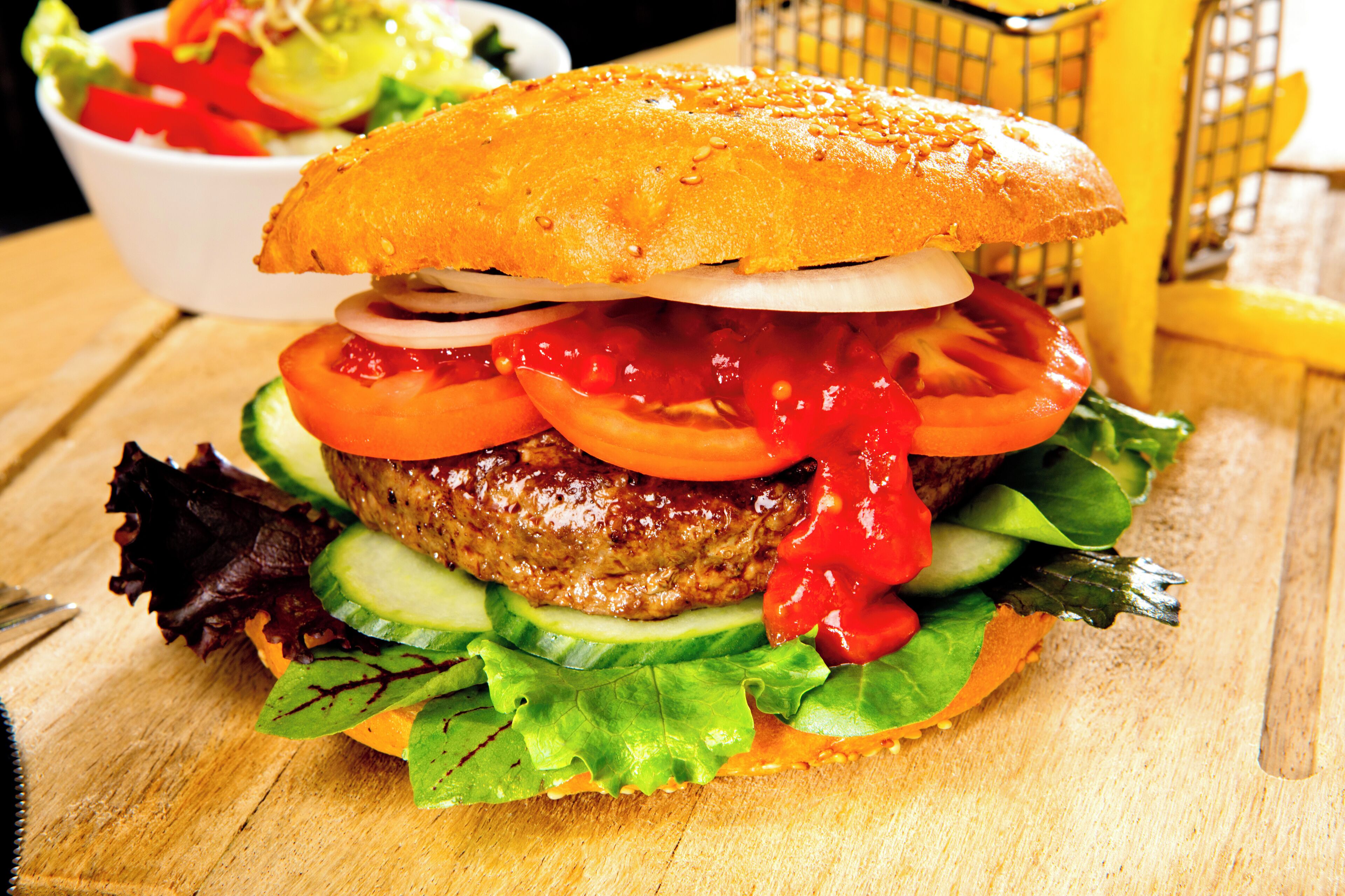 A hamburger with lettuce, tomato, and a bun on a wooden surface.