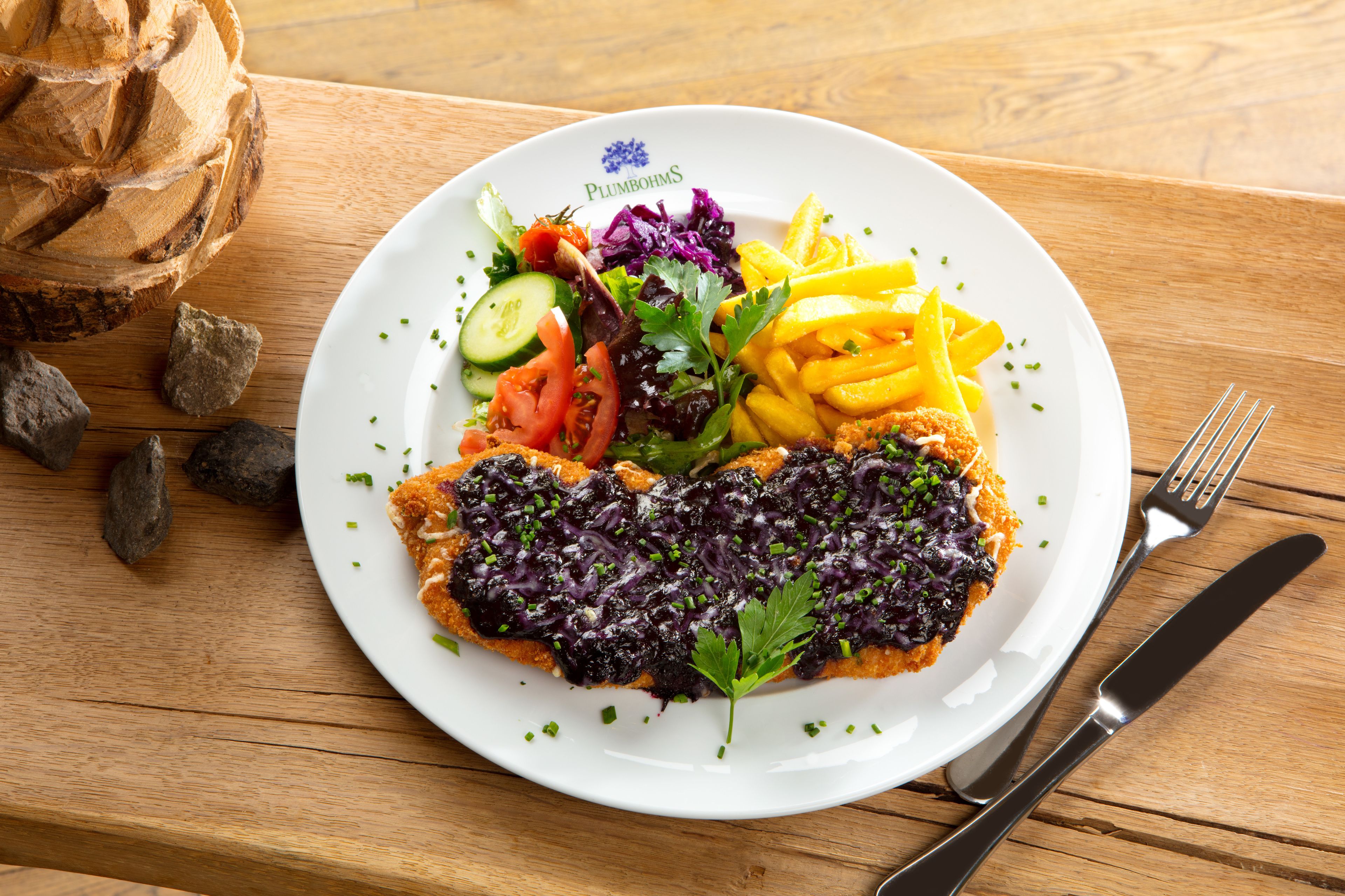 Une assiette remplie de différents légumes et d’un morceau de viande, posée sur une table en bois, avec une fourchette et un couteau à côté.