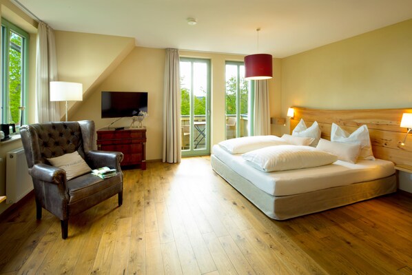 A hotel room with a bed, a leather armchair, a television, and a balcony with a view of greenery. - Aussichtsreich Gast- und Logierhaus (Bad Harzburg)