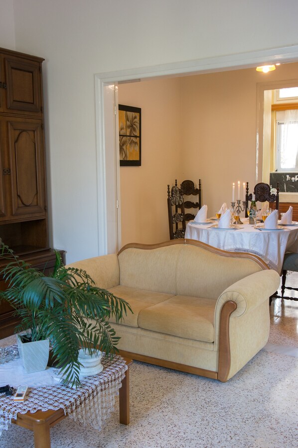 Una sala de estar con un sofá color beige, una mesita redonda con mantel de encaje y una planta en maceta.