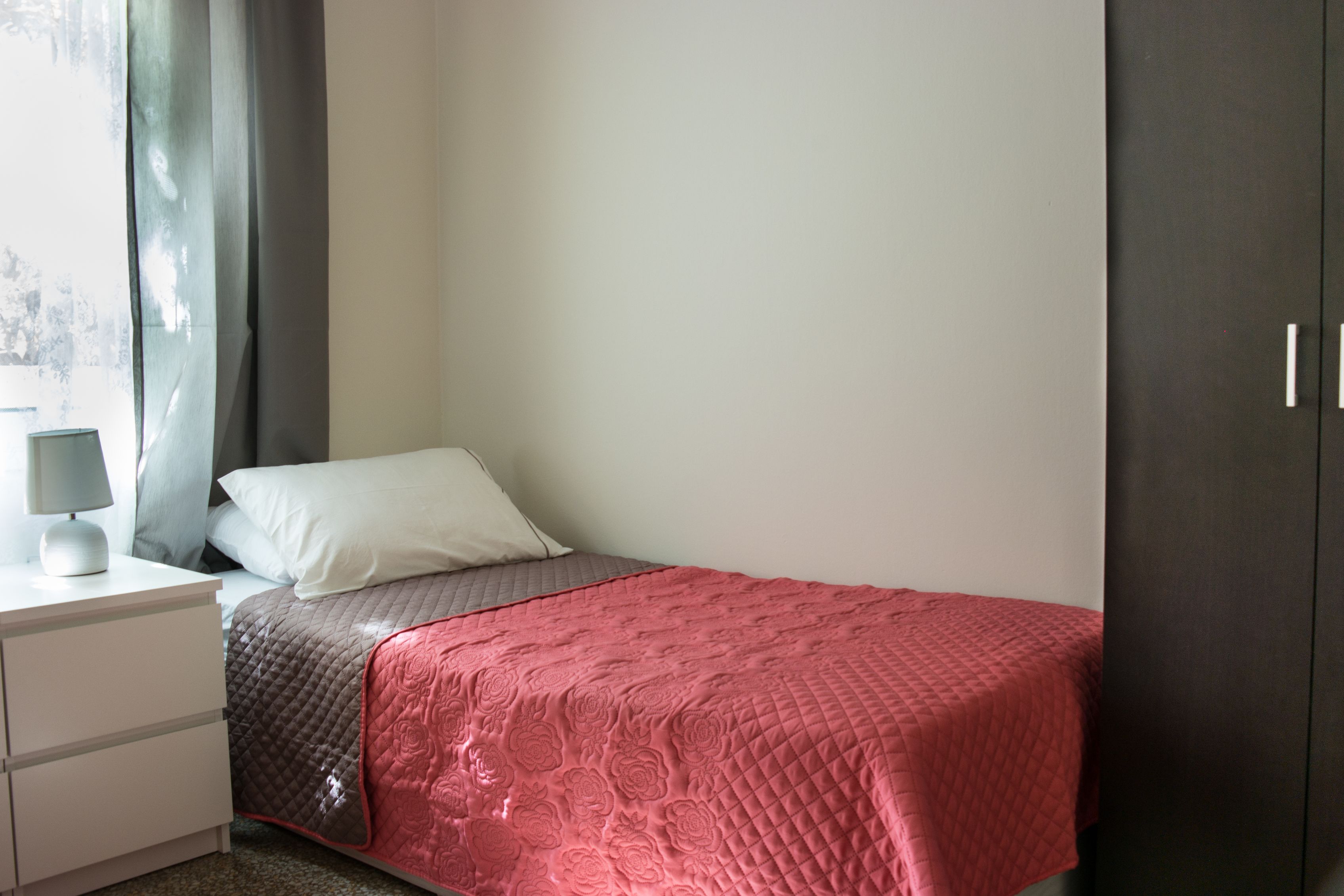 A bedroom with a bed, a nightstand, a lamp, and a wardrobe.