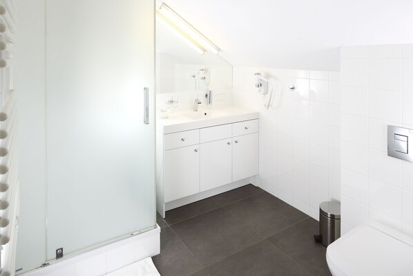 Un baño moderno con tocador blanco, espejo, secador de pelo y cubo de basura.