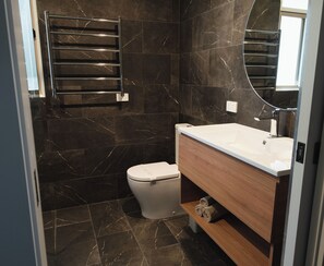 Un baño moderno con inodoro blanco, tocador de madera y salpicadero de mármol negro.