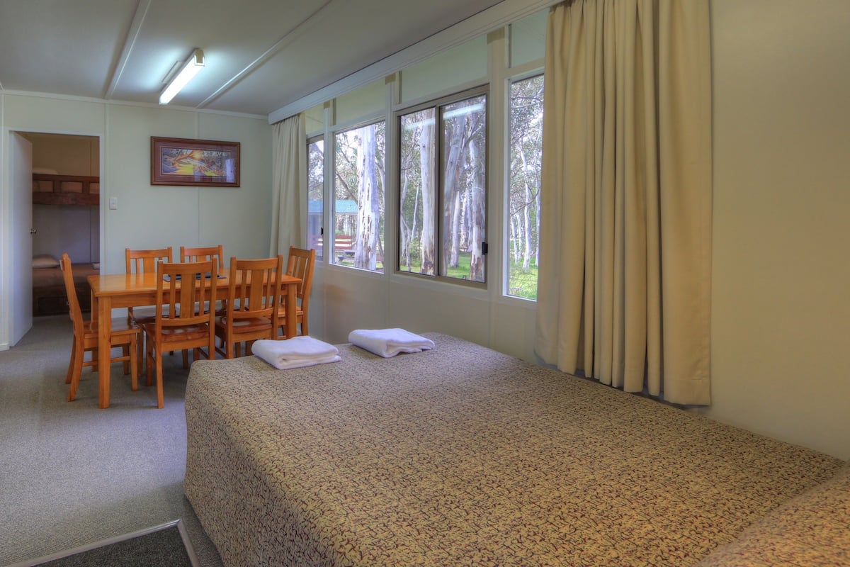 Una habitación de hotel con cama, una mesa de comedor con sillas, televisión y ventanas amplias.