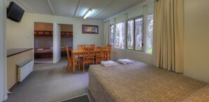 Una habitación de hotel con cama, una mesa de comedor con sillas, televisión y ventanas amplias.