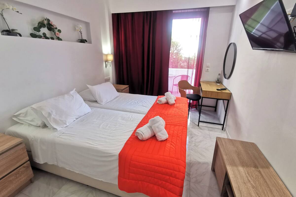 A hotel room with two beds, a desk, a chair, a TV, and a window with curtains.